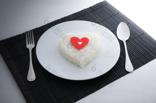 煮熟的米饭心形状与勺子和叉子在白色的盘子