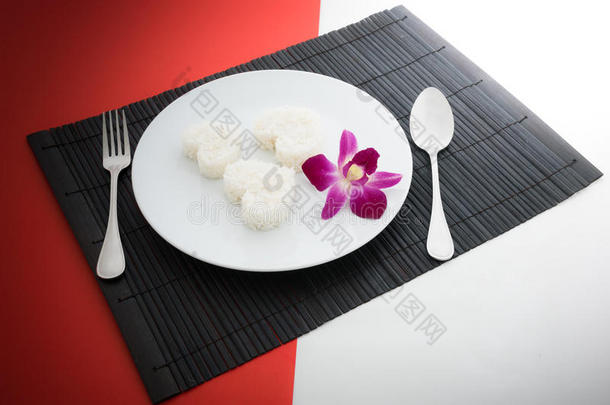 煮熟的米饭心形状与勺子和叉子在白色的盘子和
