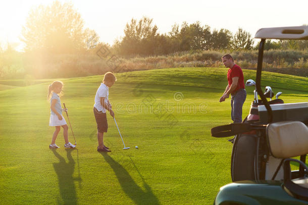 在高尔夫球场拿高尔夫俱乐部的休闲孩子。 日落