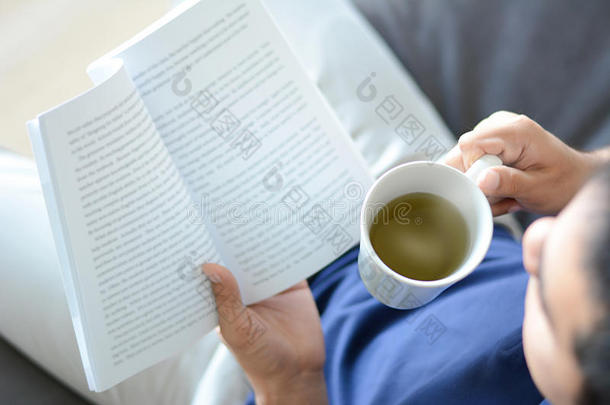 一个一只手拿着热茶杯读书的人