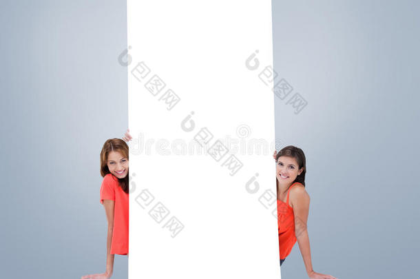 两个微笑的十几岁女孩坐在一张空白海报后面的复合图像