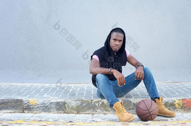 酷的年轻人坐在人行道上打篮球
