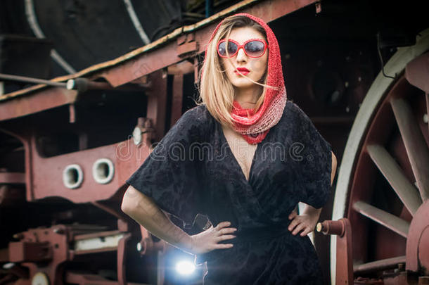 漂亮的女孩，戴着红头巾和太阳镜，在一辆老式火车前的站台上摆姿势。 女人的古董