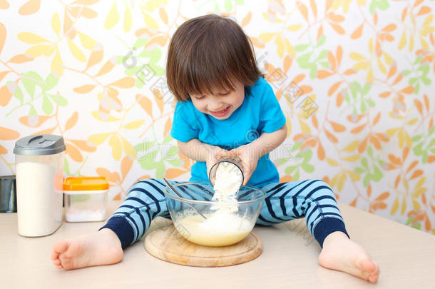 可爱的小孩子坐在家里厨房的桌子上做饭