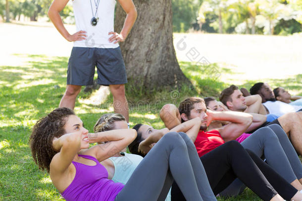 健身小组在公园和教练一起做仰卧<strong>起坐</strong>