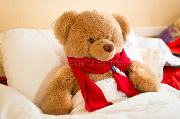 棕色泰迪<strong>熊戴</strong>着阅读<strong>围巾</strong>躺在床上，带着温度计