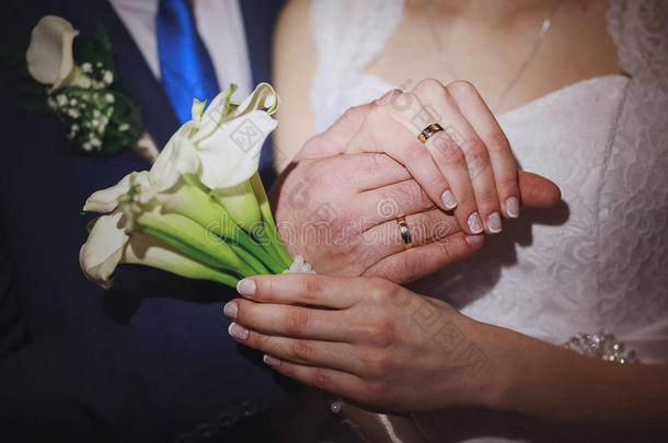 新娘夫妇的手与结婚戒指的特写。 新娘拿着白花的婚礼花束