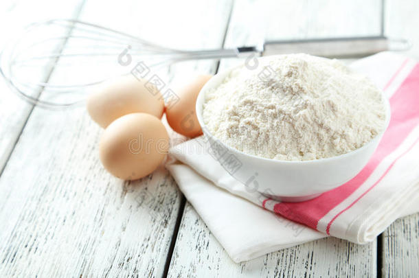 碗小麦面粉与<strong>鸡蛋</strong>和<strong>搅拌</strong>在白色的木制背景