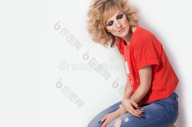 穿着牛仔裤和一件明亮的橙色T恤的漂亮女人跪在工作室的地板上，背景是白色的