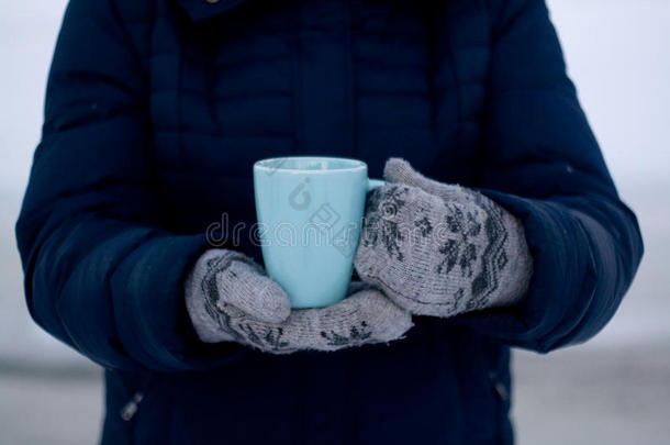 穿着蓝色羽绒服和手套的女孩拿着一杯茶