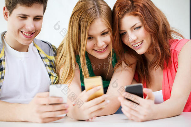 三个微笑的学生在学校拿着智能<strong>手机</strong>