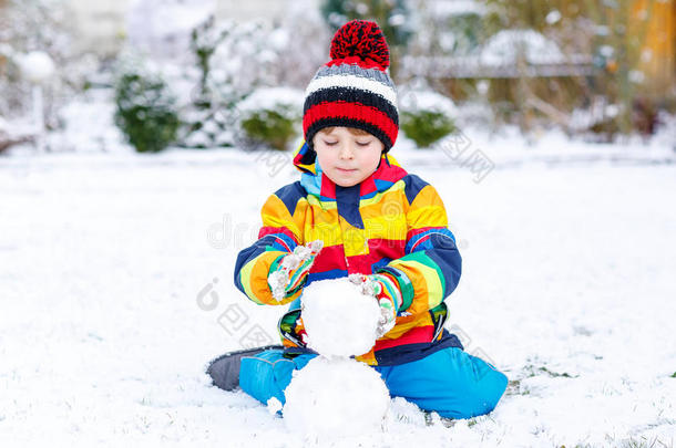 有趣的学龄前男孩穿着五颜六色的衣服堆雪人