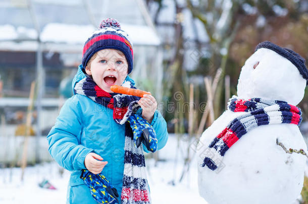 有趣的男孩穿着五颜六色的衣服在户外堆雪人