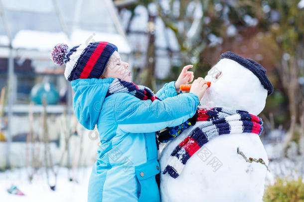 有趣的男孩穿着五颜六色的衣服在户外堆雪人