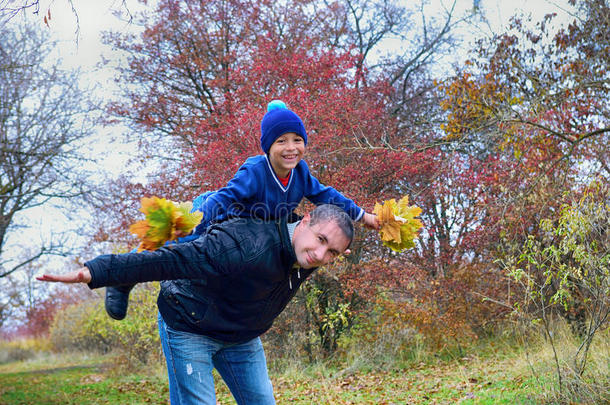爸爸在秋天的公园里背着他的儿子