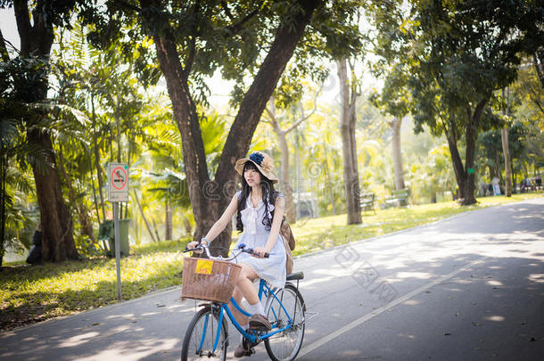 穿着老式服装的可爱的亚洲泰国女孩正在阳光明媚的夏季公园骑自行车