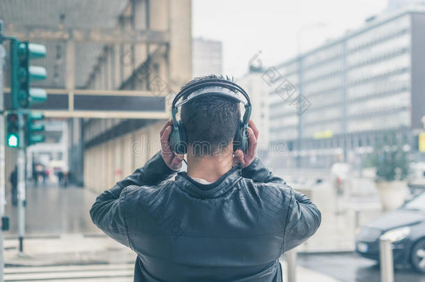 一个戴着耳机的年轻人在城市街道上摆姿势的<strong>背影</strong>