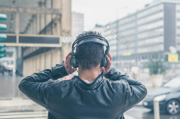 一个戴着耳机的年轻人在城市街道上摆姿势的背影