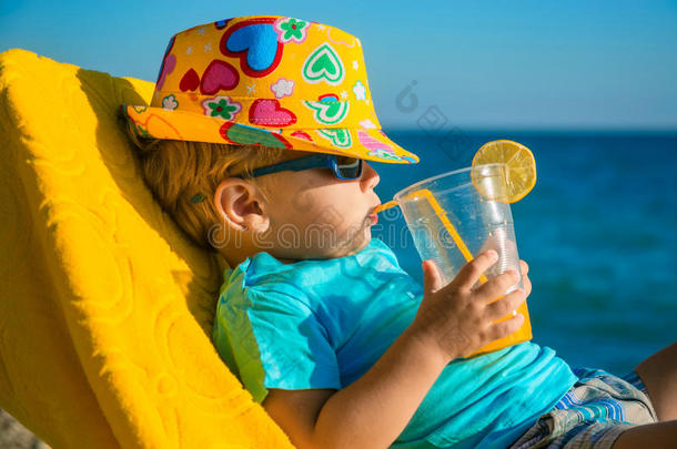 沙滩上坐在扶手椅上拿着果汁杯的男孩