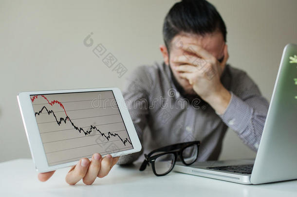 沮丧的商人把头靠在坏股票市场图表下面