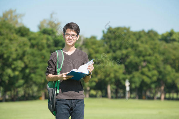 英俊的男孩拿着一本打开的书，阅读背景夏天的绿色