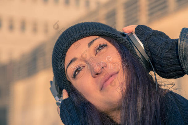 美丽的年轻女人在城市的街道上听音乐