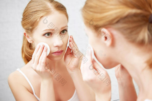 美丽的年轻女人用镜子里的面部皮肤卸妆