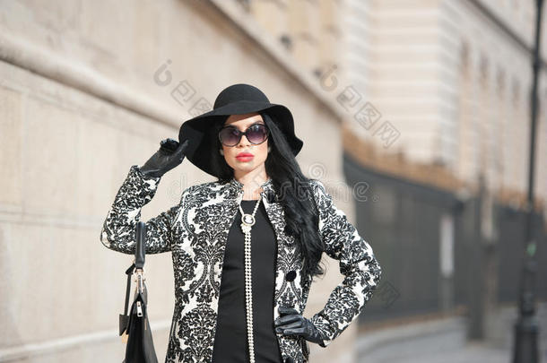 穿着冬季时装的迷人的年轻女子。美丽时尚的黑衣少女在大街上摆姿势。优雅的黑发女郎