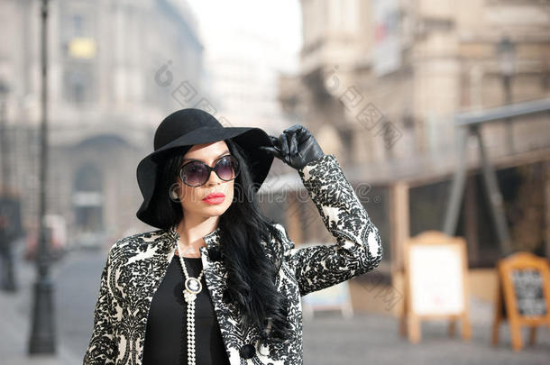 穿着冬季时装的迷人的年轻女子。美丽时尚的黑衣少女在大街上摆姿势。优雅的黑发女郎