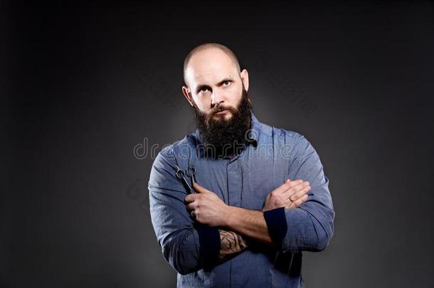 一个留胡子的秃头男人手里拿着一把剪刀。双手交叉放在胸前