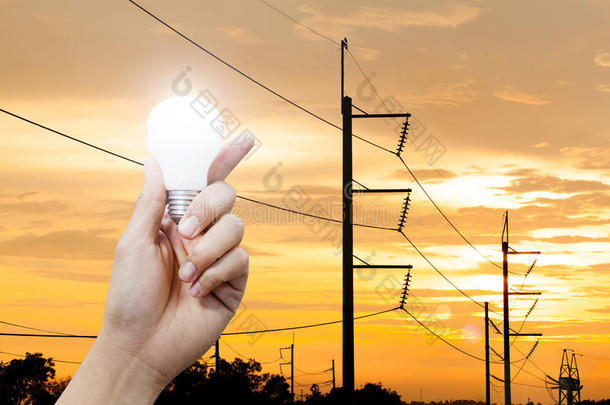 手拿着一个发光的灯泡和电线杆日落背景