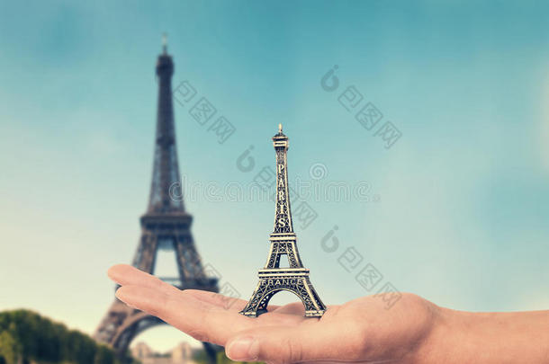 手拿着埃菲尔铁塔纪念品玩具，背景是真正的埃菲尔铁塔