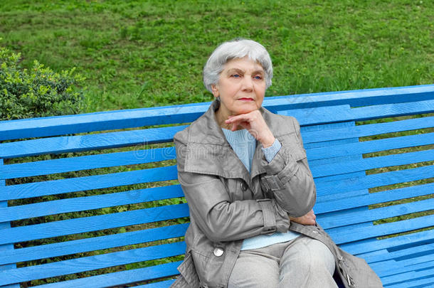 美丽可爱的老妇人坐在公园长凳上蓝色