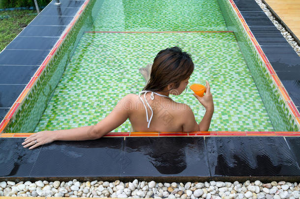 亚洲女孩在游泳池里喝杯橙汁