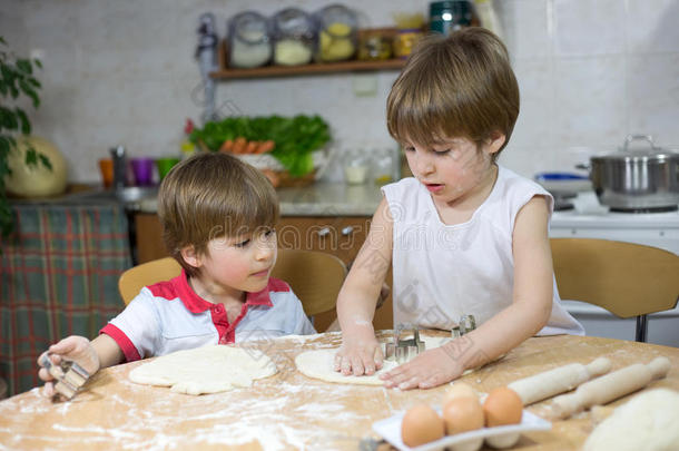 可爱的小<strong>男孩</strong>教他的孪生兄弟如何在厨房的桌子上平面团