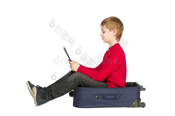 男孩坐在旅行袋使用平板电脑隔离在白色