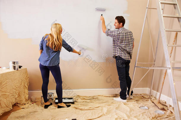夫妇装饰室使用油漆滚筒在墙上