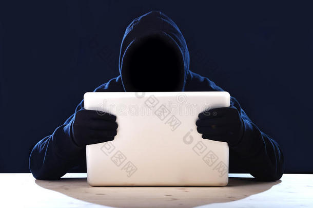 黑客男子在黑色引擎盖和面具与电脑笔记本电脑黑客系统在数字入侵者网络犯罪的概念