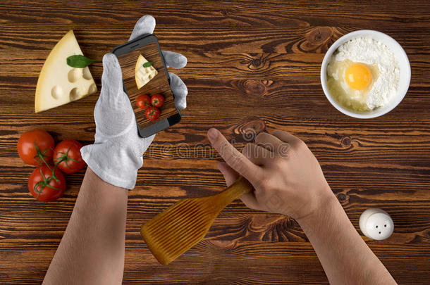 厨师手与智能手机和食材的食物在老式木制背景纹理