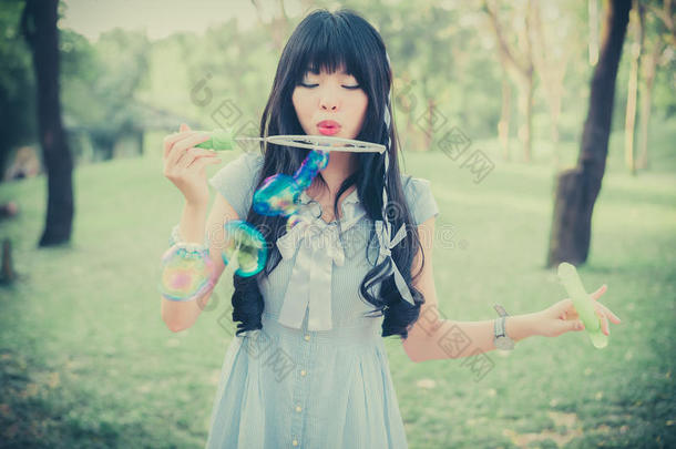 可爱的亚洲泰国女孩正在博士公园里吹肥皂泡