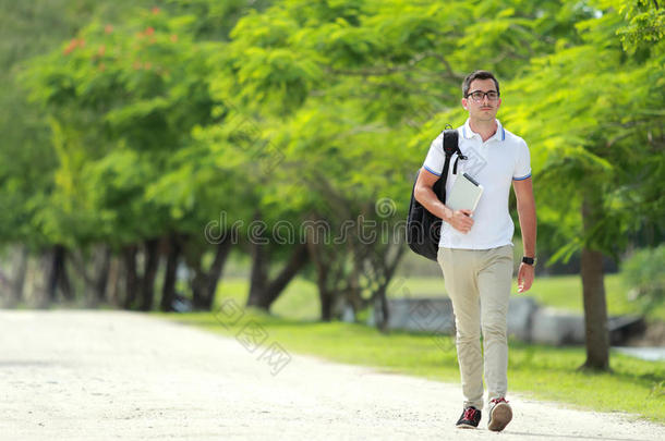 英俊的大学生带着背包和平板电脑在大学公园散步