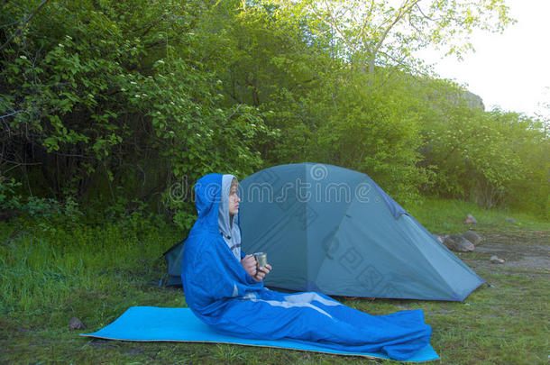 一个男人坐在帐篷附近的睡袋里。