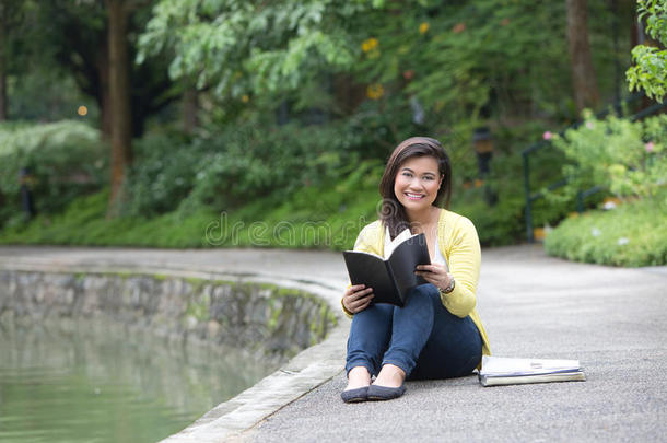 女大学生或大学生，坐在公园的湖边。