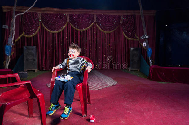 穿着小丑<strong>化妆</strong>的男孩坐在舞台上的<strong>椅子</strong>上