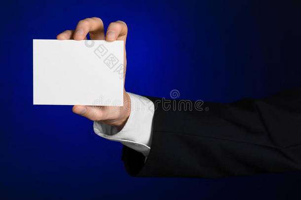 <strong>商业</strong>和广告主题：穿着黑色西装的男人手里拿着一张白色的空白卡，<strong>背景</strong>是深<strong>蓝色</strong>的工作室