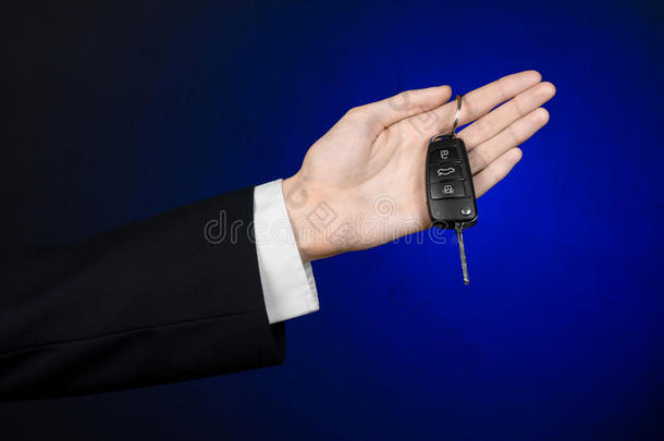 商业和礼物<strong>主题</strong>：穿着黑色西装的<strong>汽车</strong>推销员在工作室的深蓝色背景上拿着一辆新车的钥匙