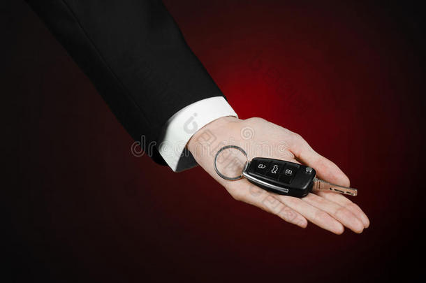 商业和礼物<strong>主题</strong>：穿着黑色西装的<strong>汽车</strong>推销员在工作室的深红色背景上拿着一辆新车的钥匙