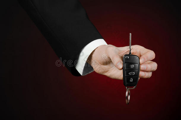 商业和礼物主题：穿着黑色西装的汽车推销员在工作室的深红色背景上拿着一辆新车的钥匙