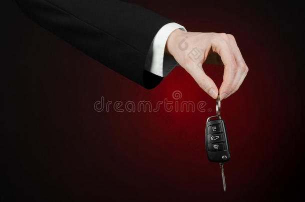 商业和礼物<strong>主题</strong>：穿着黑色西装的<strong>汽车</strong>推销员在工作室的深红色背景上拿着一辆新车的钥匙