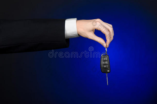 <strong>商业</strong>和礼物主题：穿着黑色西装的汽车推销员在工作室的深<strong>蓝色背景</strong>上拿着一辆新车的钥匙